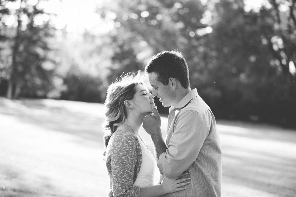 Romantic couple shares tender moments in a sunlit park setting with soft bokeh background.