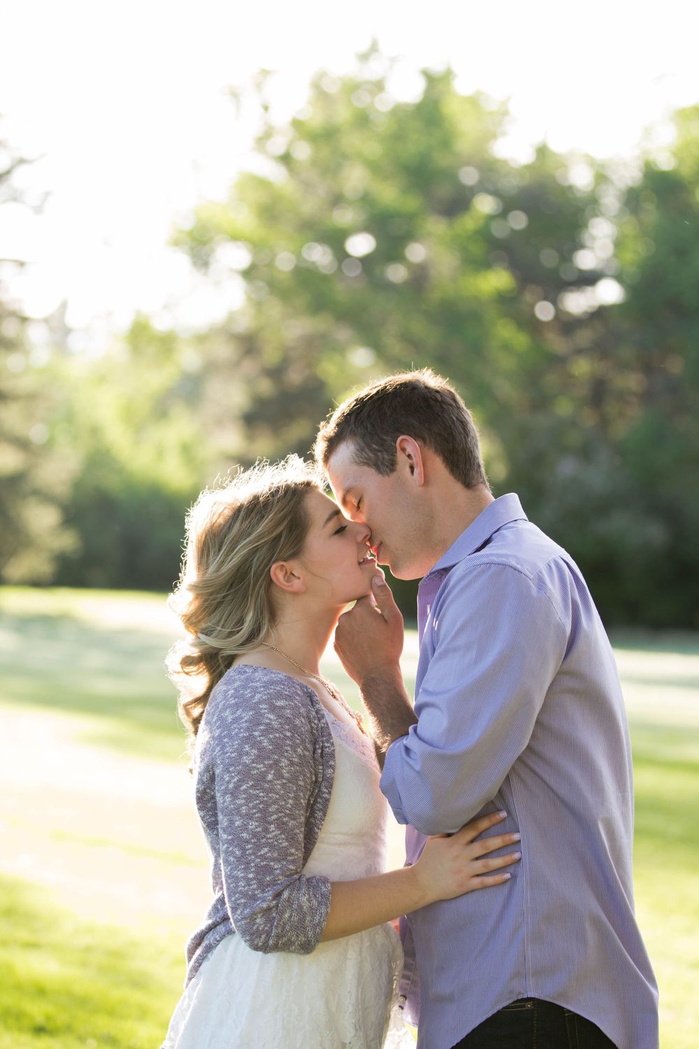 A romantic couple embraces during a sunset photoshoot in a grassy park setting.