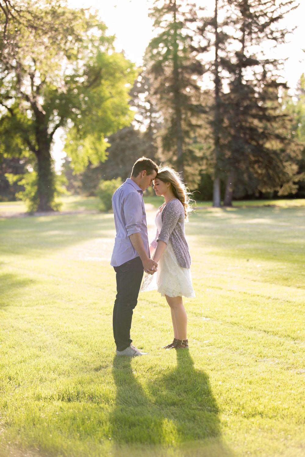 A couple shares tender moments in a sunlit park during a romantic photoshoot.
