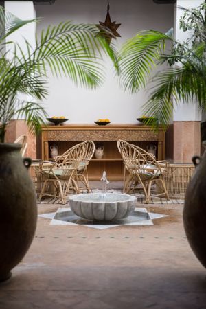 Tranquil courtyard setting with rattan chairs, palm fronds, and decorative fountain.