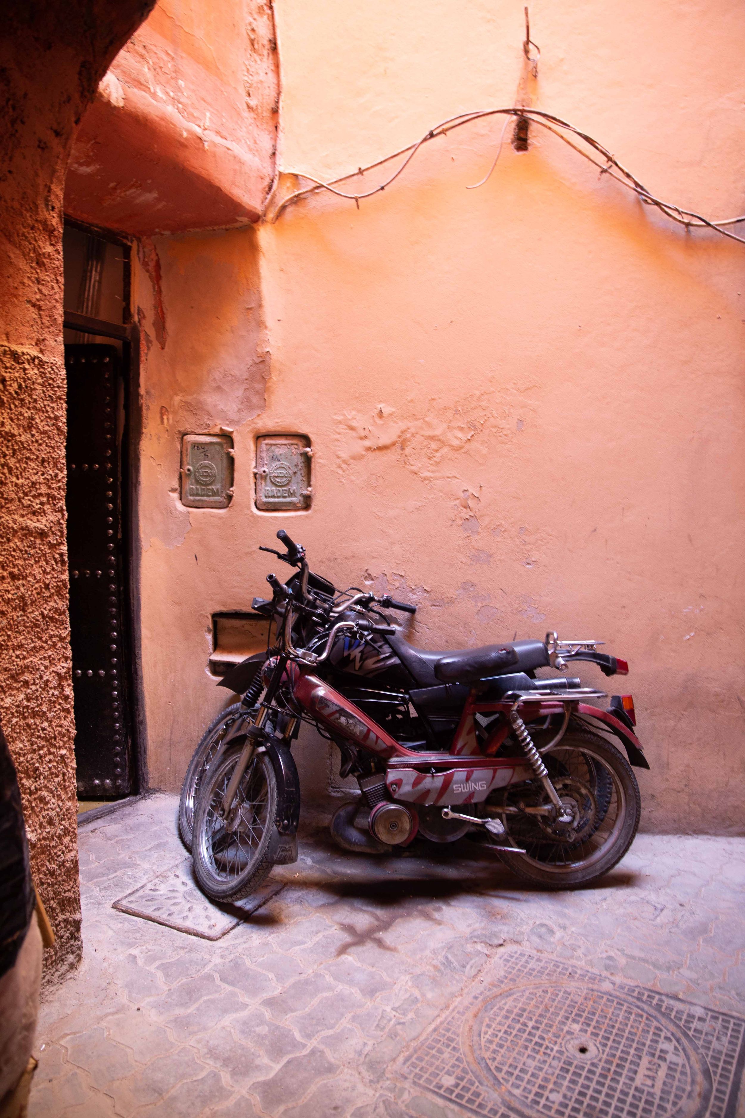 Motorcycle parked against coral-colored wall in narrow Moroccan alley.