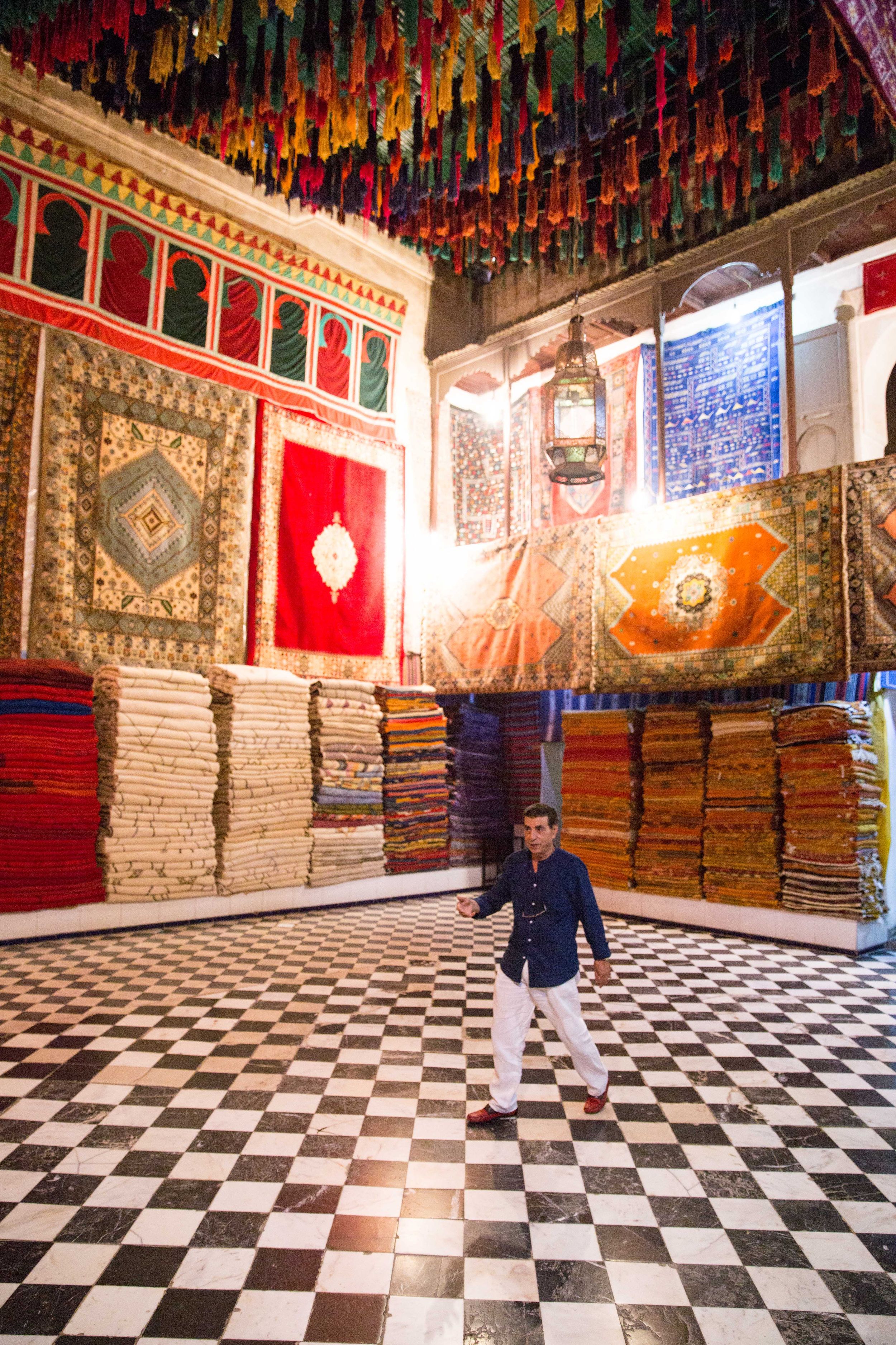 Traditional Moroccan carpet shop with colorful rugs and checkered floor pattern.