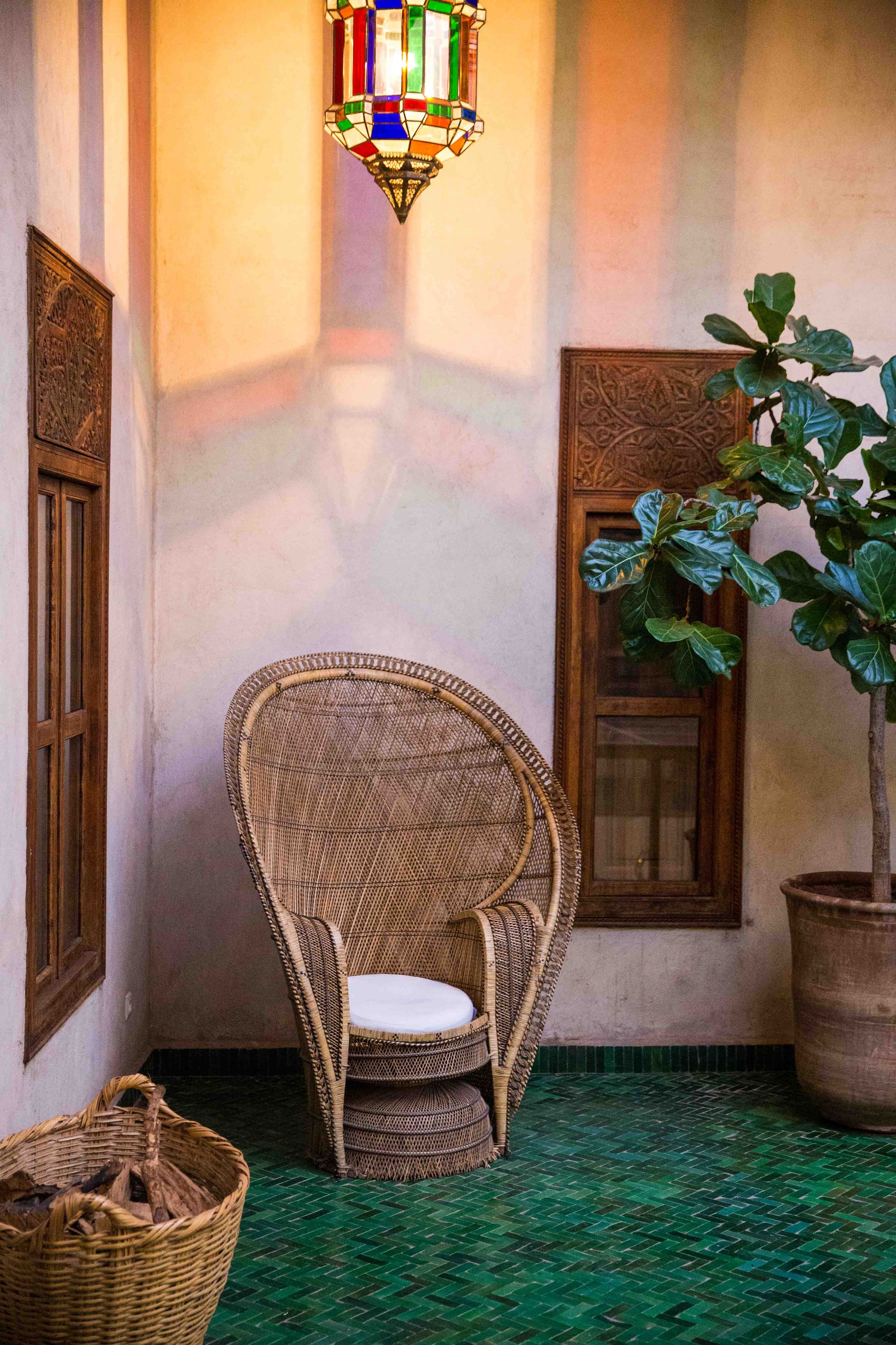 Cozy corner with wicker peacock chair, colorful lantern, and potted plant on green tiled floor.