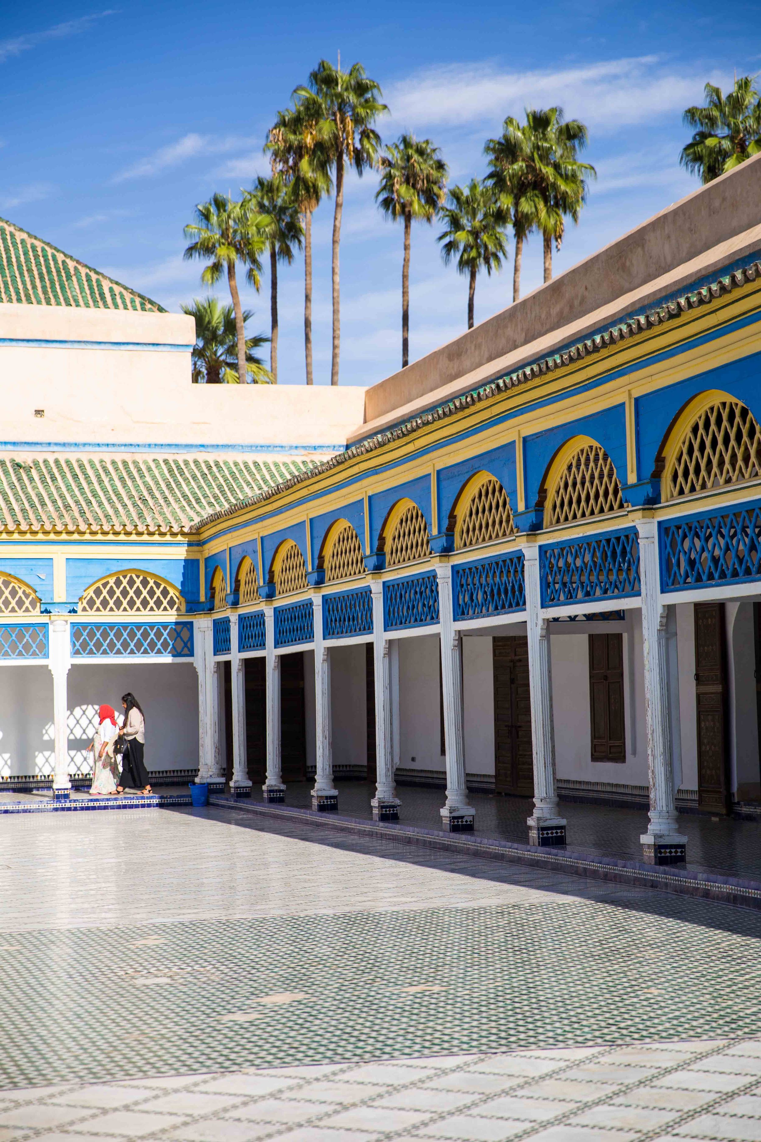 Moroccan courtyard with blue and white archways, palm trees, and traditional architecture.