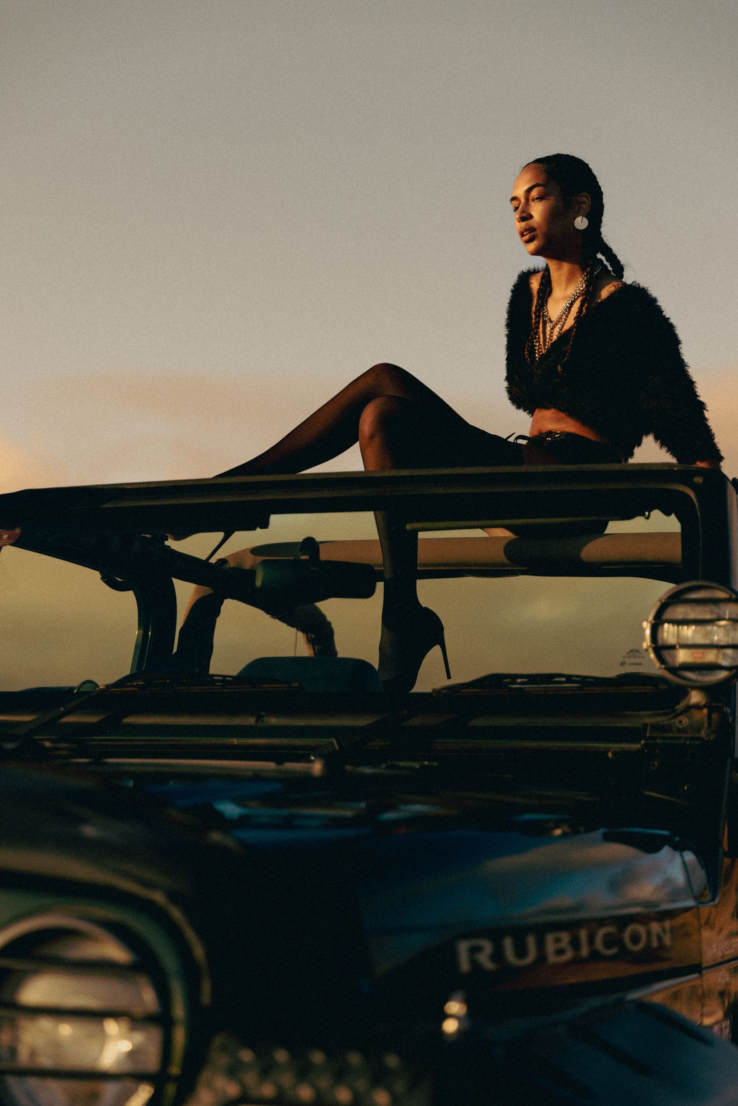 Model in black poses on Jeep Rubicon during golden hour sunset.