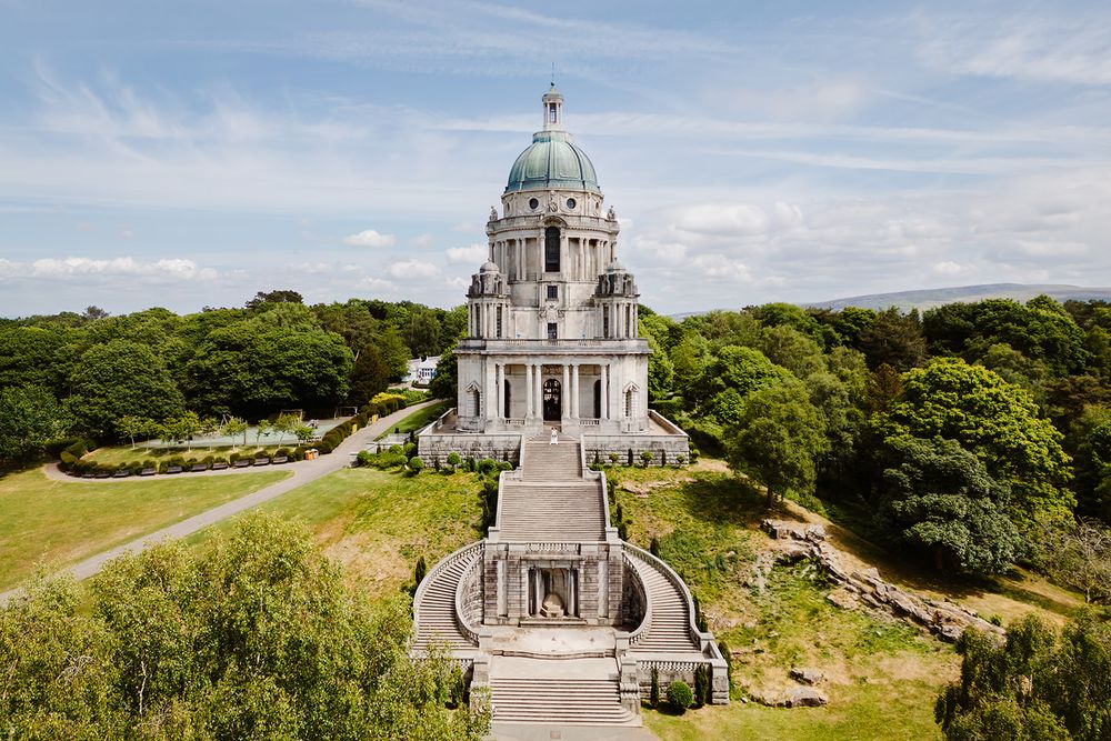 Aerial view of the Ashton Memorial, a grand baroque monument with green dome, surrounded by lush trees in Williamson Park, Lancaster.