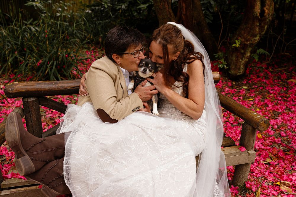 Two brides with their dog at Briery Wood Country House Hotel. Romantic portrait under the colourful rhododenrons