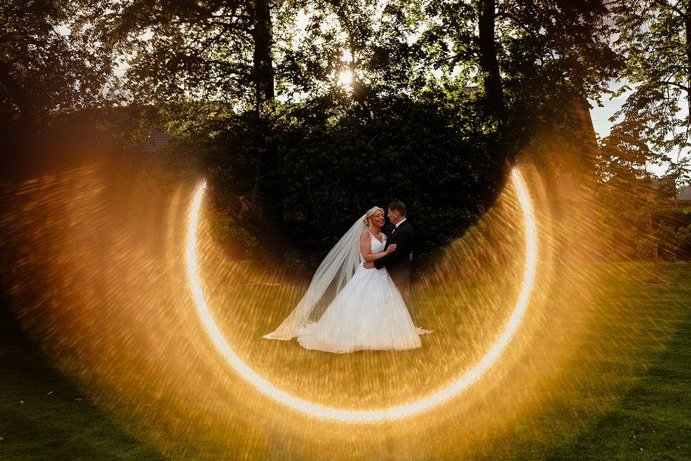 Bride and groom share romantic kiss surrounded by glowing circular light art in lush garden at golden hour.