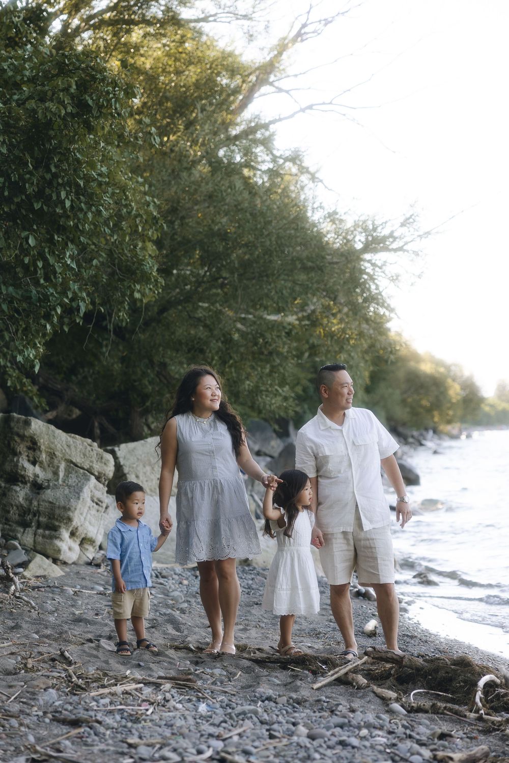 A family strolls together on a rocky lakeside beach path with lush greenery behind them.
