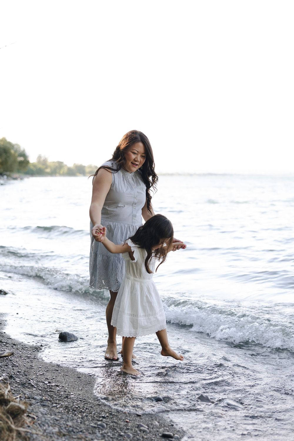 Mother and child play joyfully at the water's edge on a rocky beach at sunset.