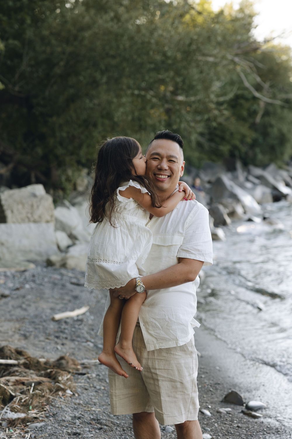 A heartwarming moment between two people embracing by a rocky shoreline on a sunny afternoon.