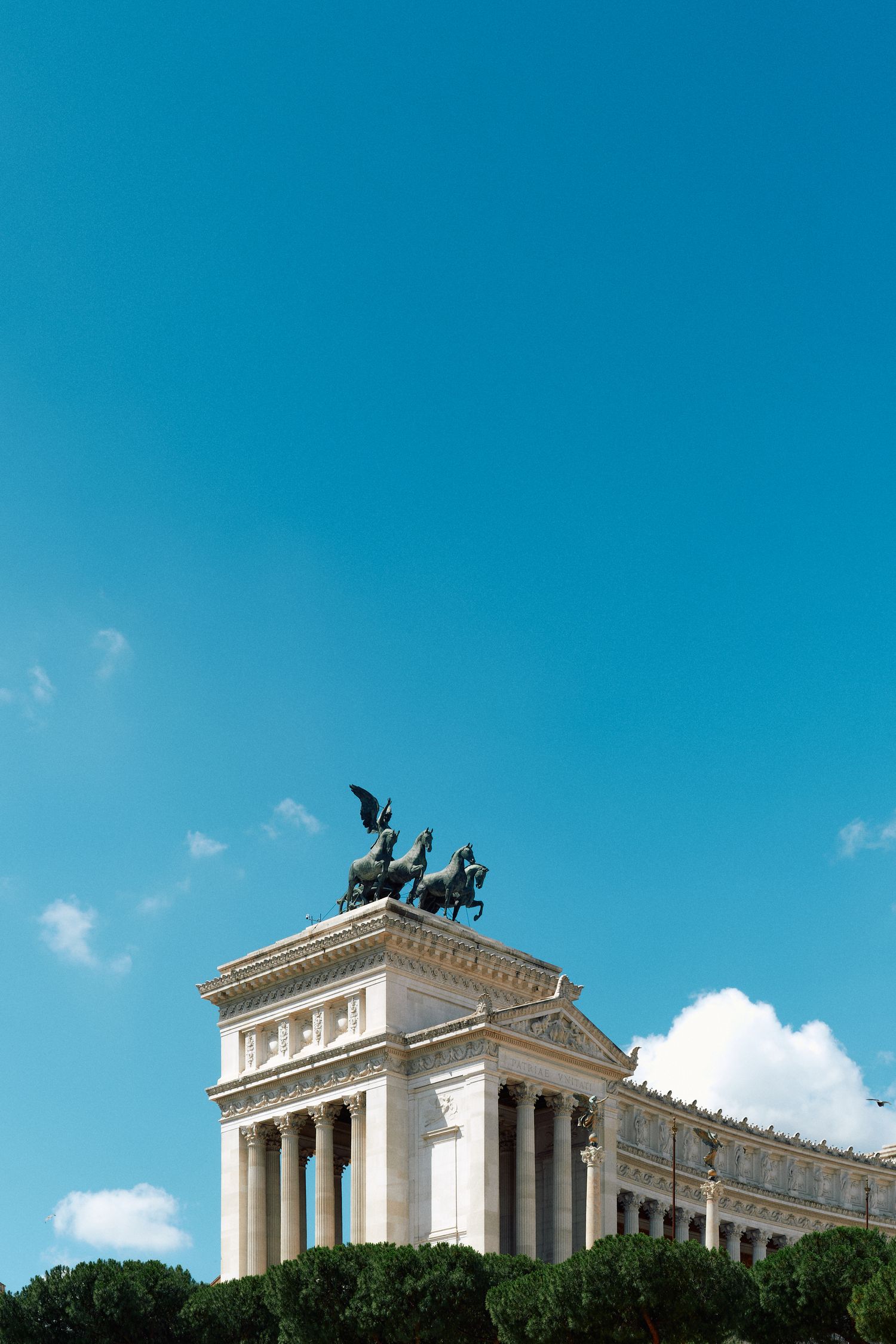 Ornate neoclassical building with sculptures on top against bright blue sky.