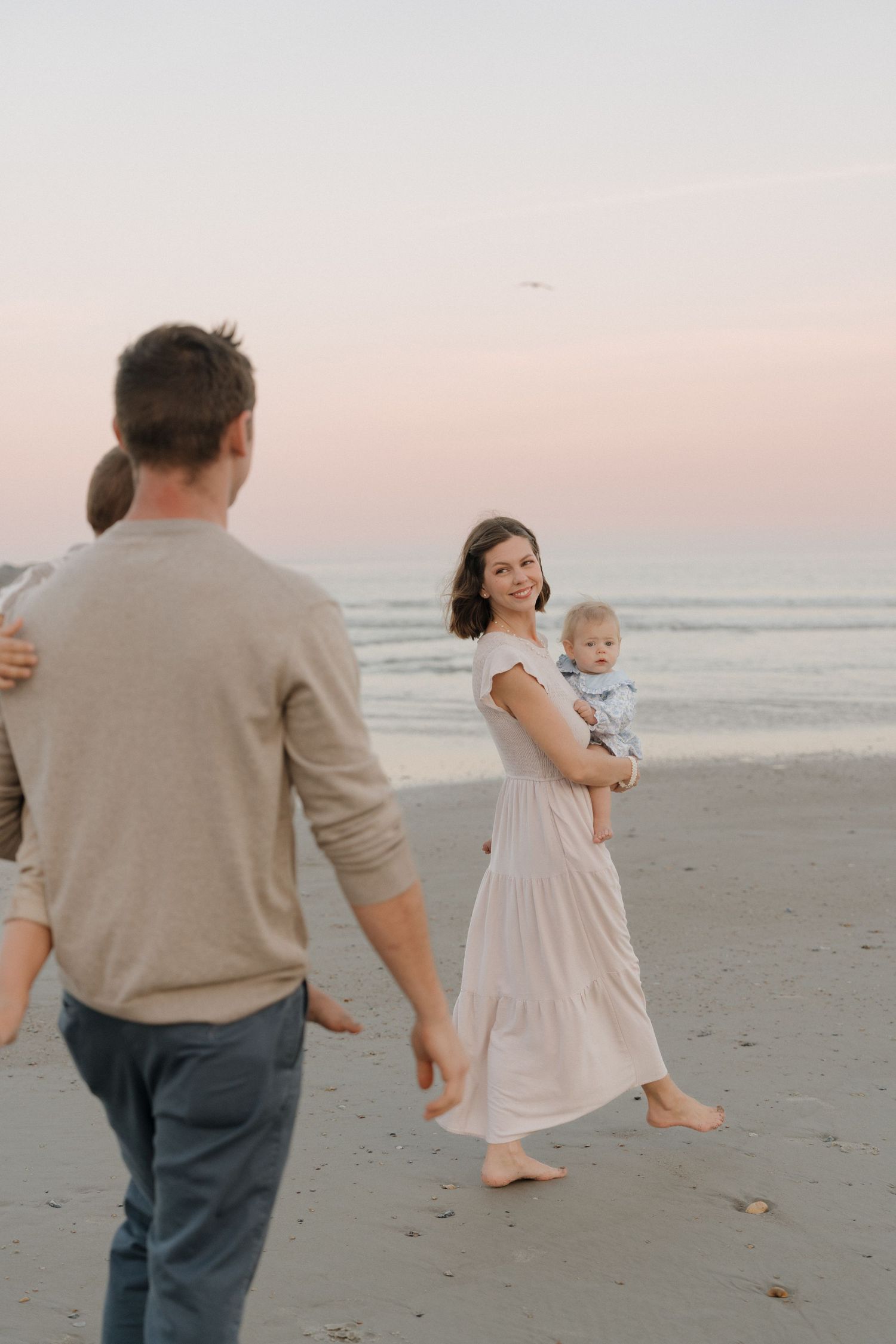 Artistic maternity photo of woman in water during golden hour at rocky beach.