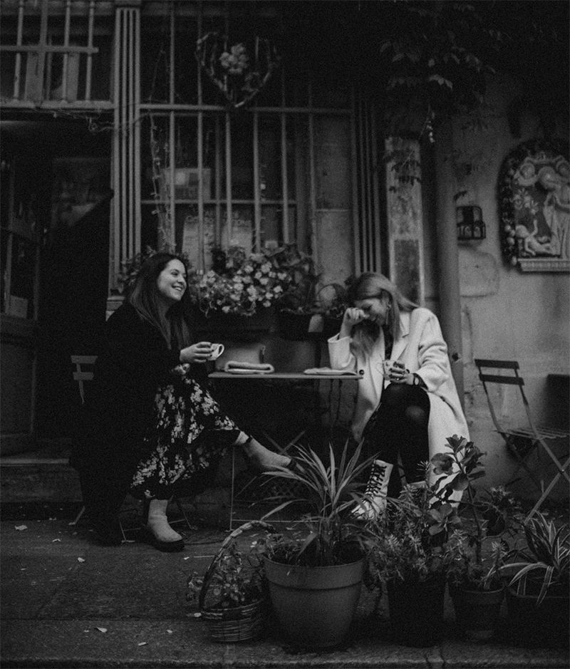 Vintage black and white photograph of friends relaxing at outdoor cafe with plants.