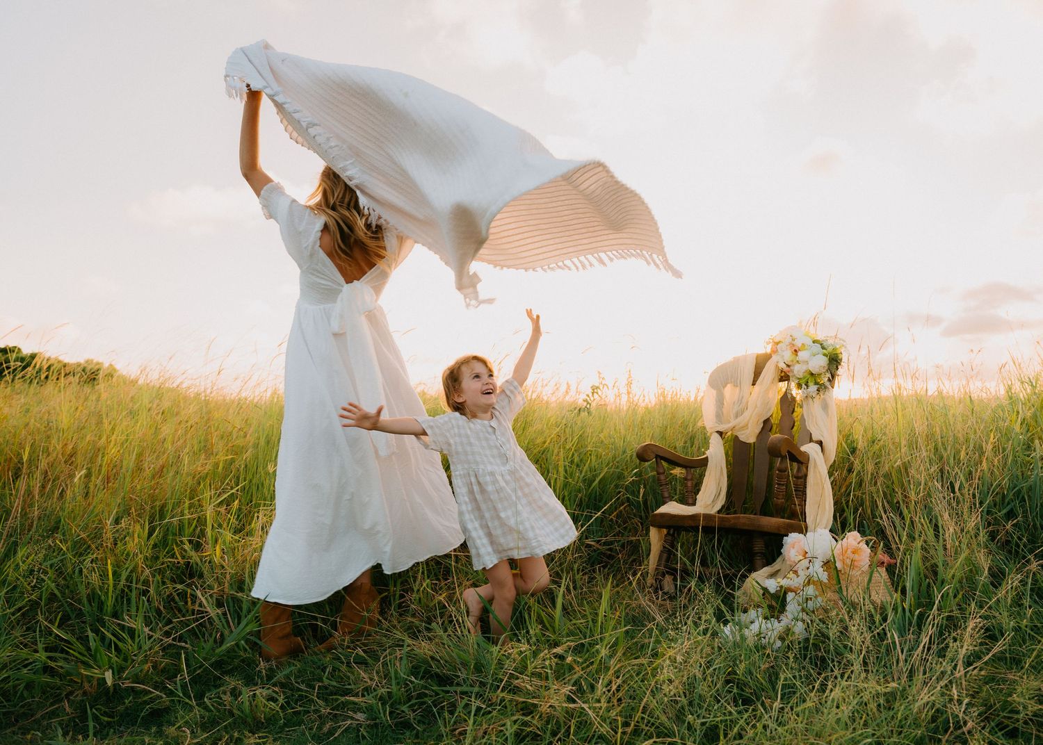 Women and children playing with flowing white fabric in sunlit meadow.