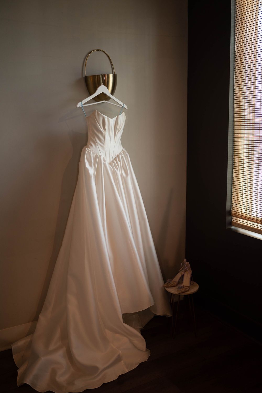 White wedding dress hanging on display in a dimly lit room near a window.