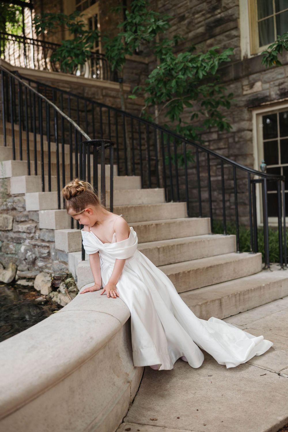 Bride in white gown poses gracefully on stone steps with iron railing.