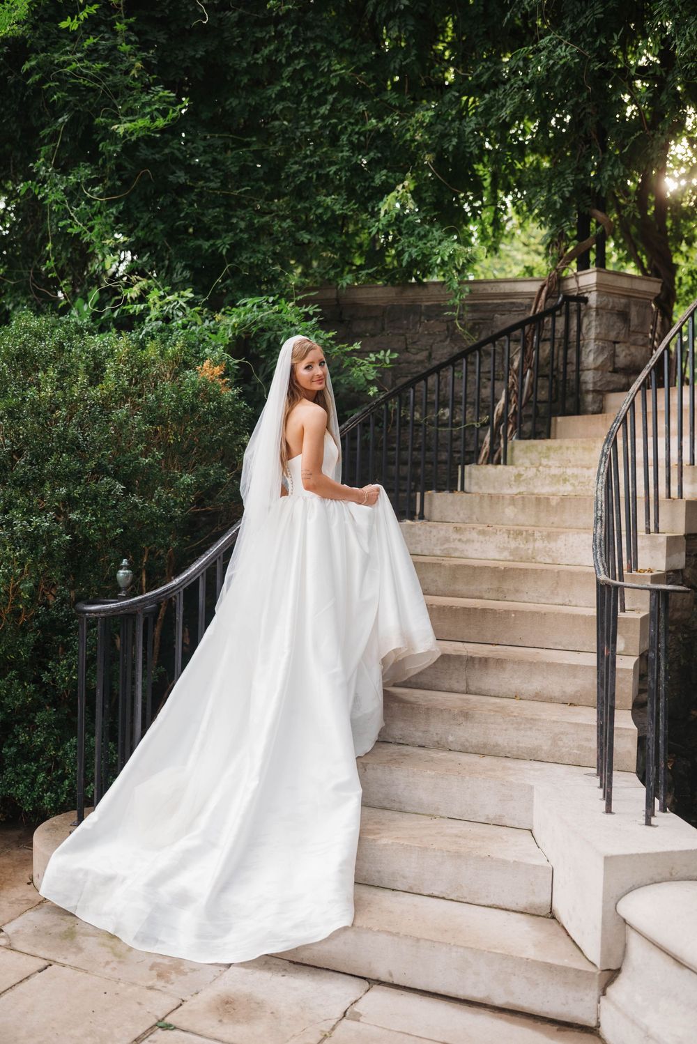Wedding dress train flows elegantly down outdoor stone staircase.