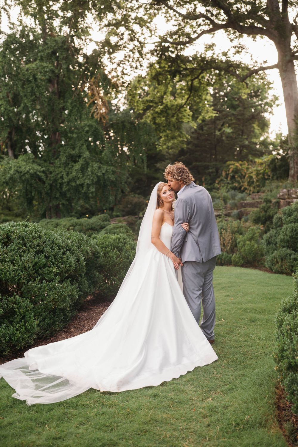 Newlyweds embrace on grassy hillside during sunset photo session.