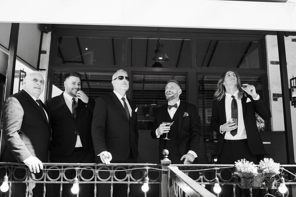 Groomsmen laughing and celebrating on decorated balcony in black and white photo.