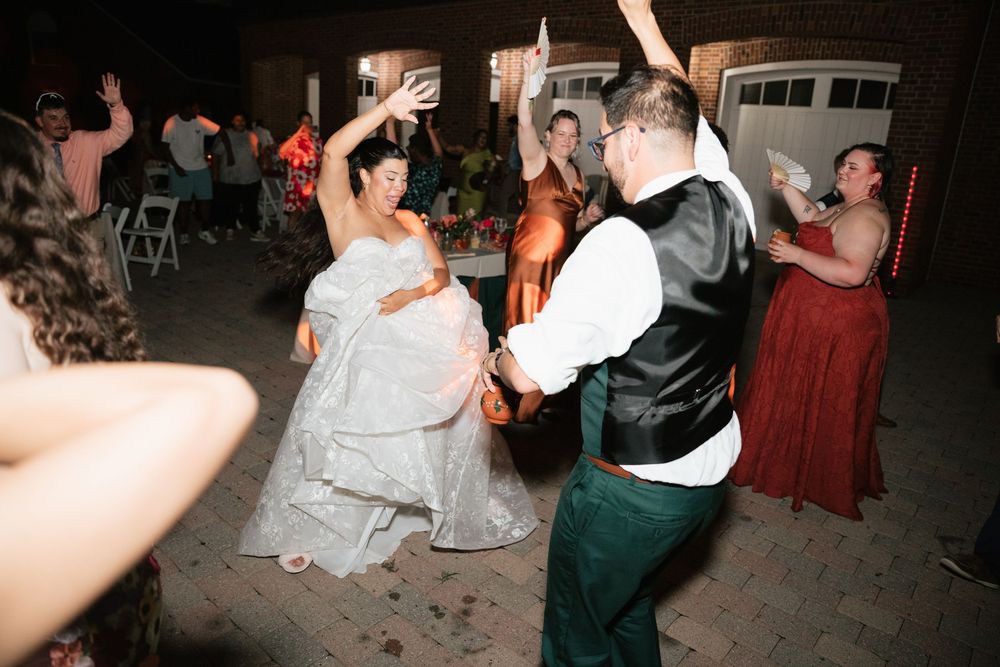 Bride and groom dancing joyfully with guests at an outdoor wedding reception at night.