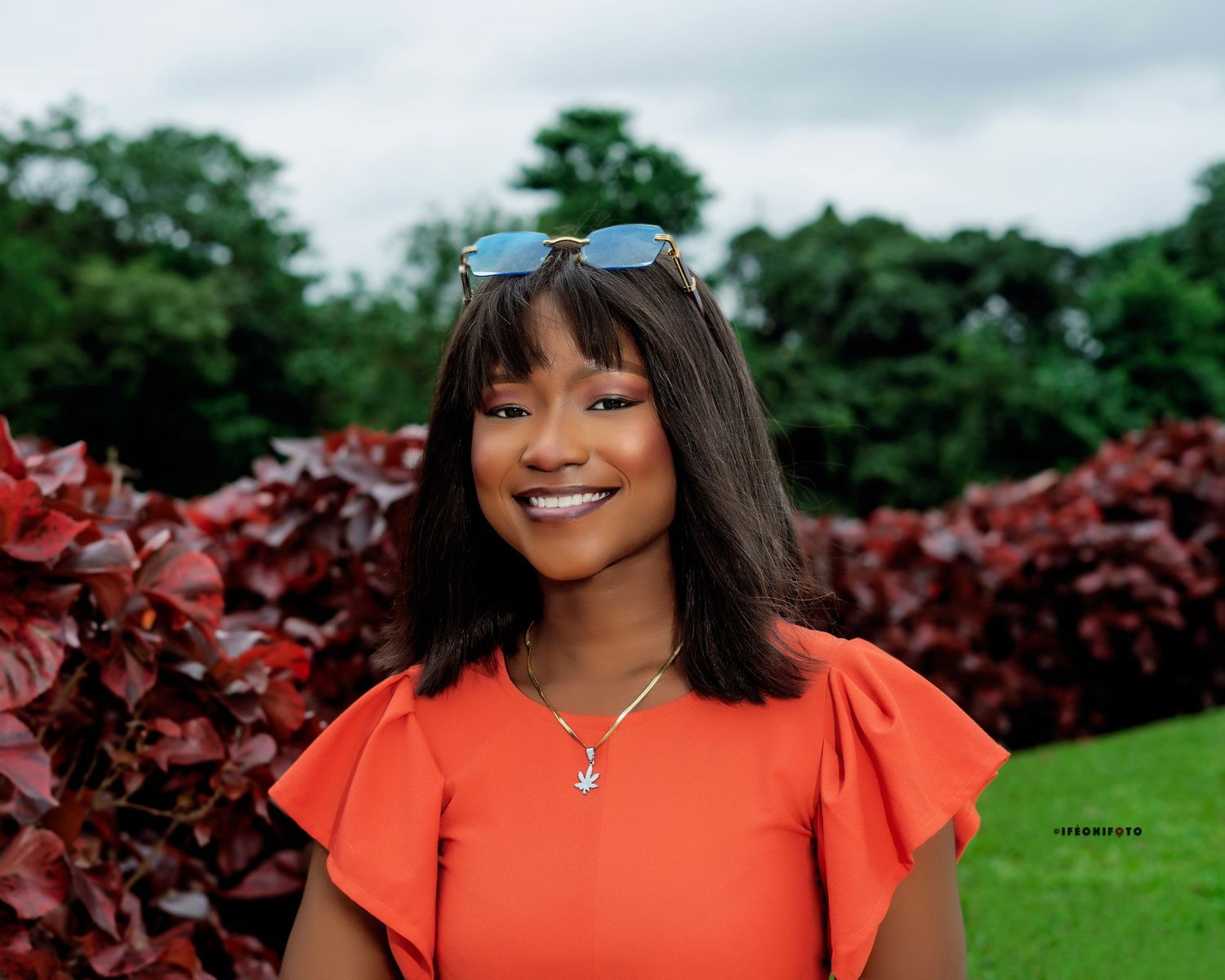 A beautiful young woman in a radiant smile, wearing an orange dress in an outdoor shoot captured by ifeonifoto.