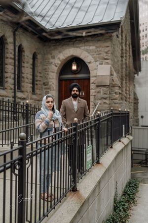Couple standing by iron railing outside historic stone church with arched doorway.