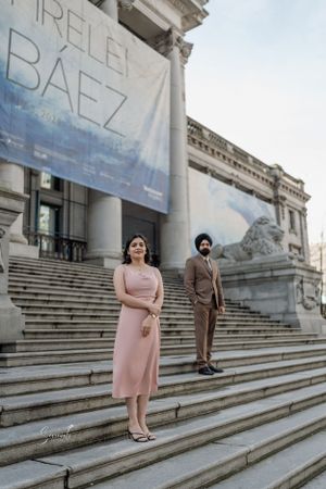 Couple posing on grand stone steps with classical architecture and banner.