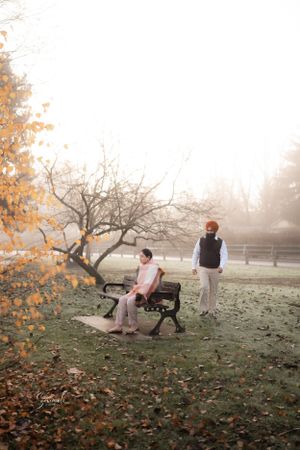 Two people in a misty autumn park with fallen leaves and bare trees.