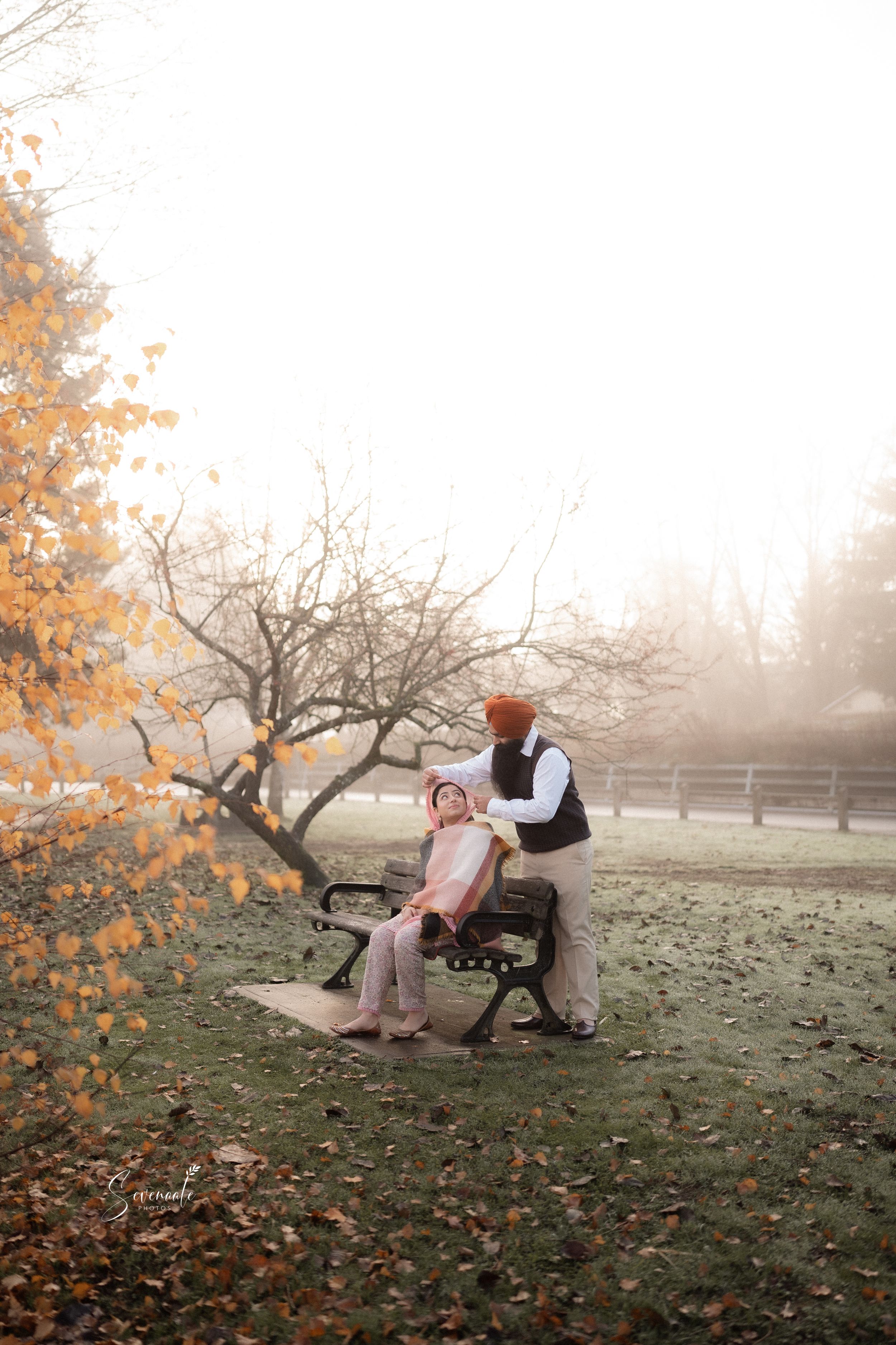 Couple sitting on park bench surrounded by autumn foliage in misty weather.