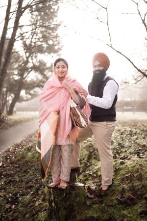 Couple in traditional Punjabi attire pose together in misty autumn park setting.