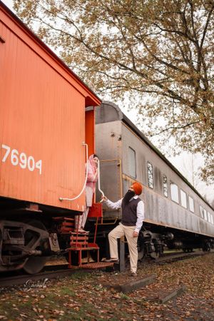 A vintage train car numbered 76904 with steps being climbed on an autumn day with fallen leaves.