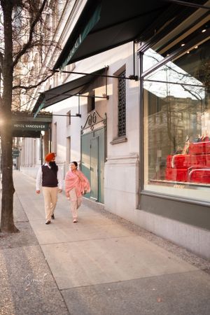 A couple walks past storefront windows on a city sidewalk during autumn.