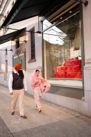 A couple strolling past retail shop windows on an urban street.