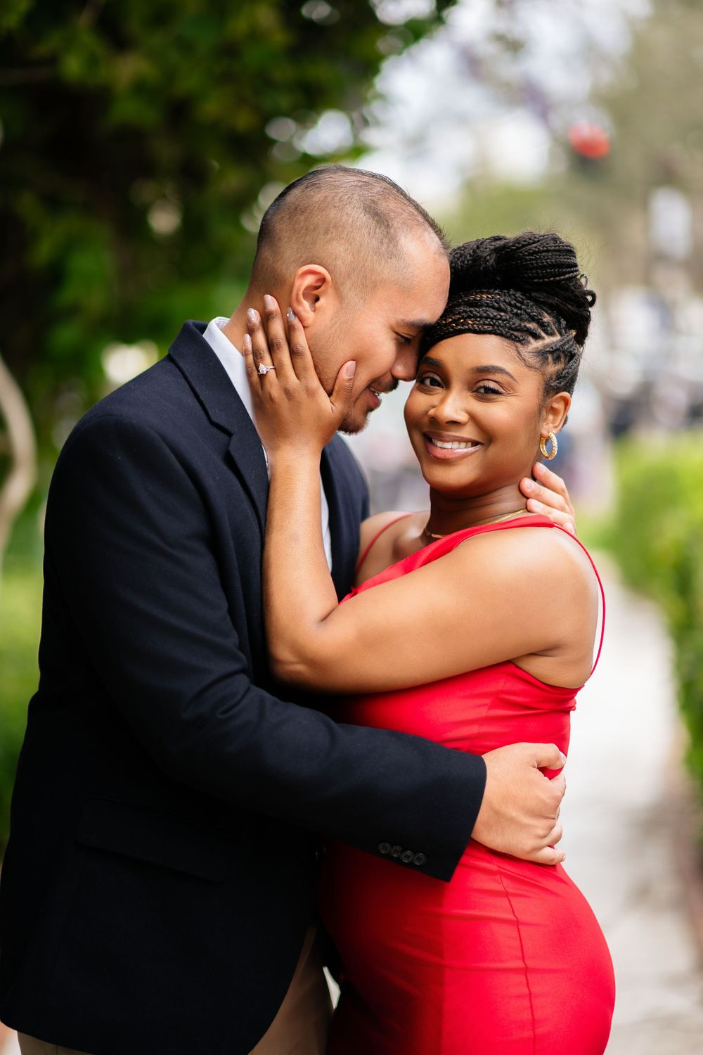 Romantic couple embracing outdoors, dressed in formal red dress and black suit.