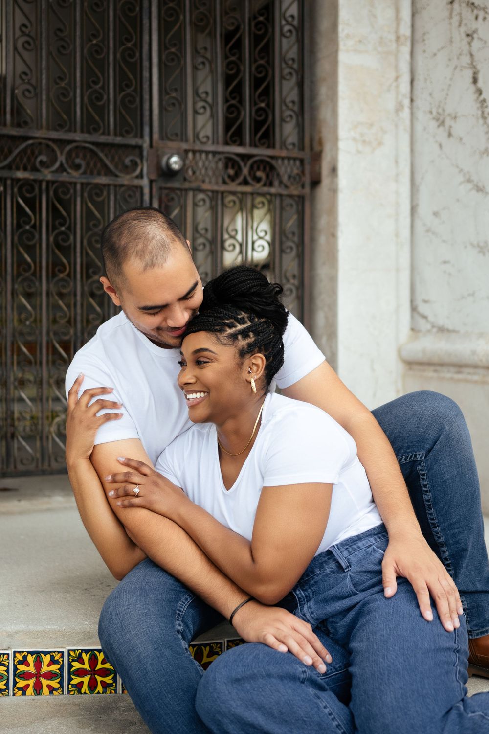 Couple in white shirts and jeans sharing intimate moment on vintage steps.