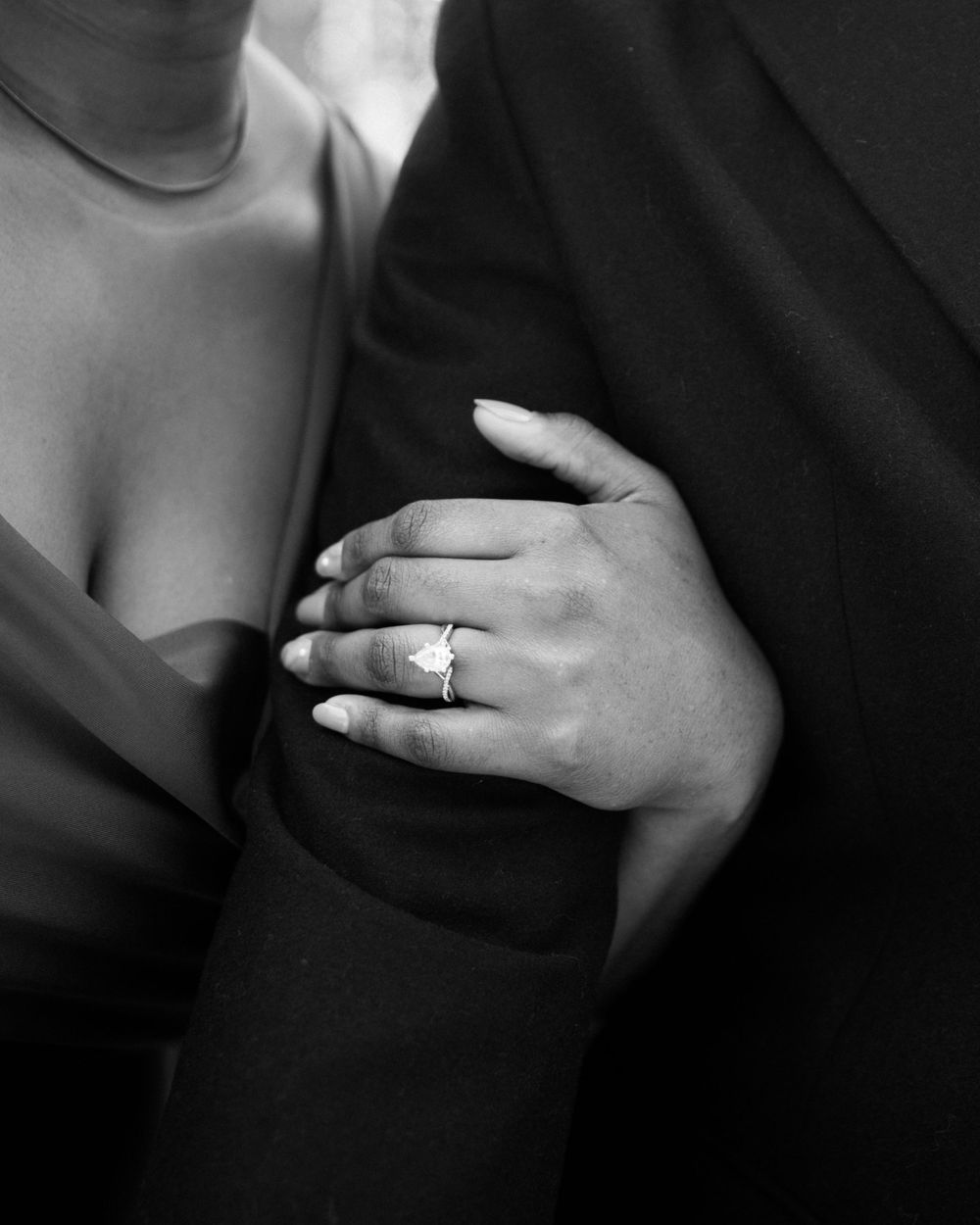 Close-up of hands showing engagement ring while embracing in formal wear.