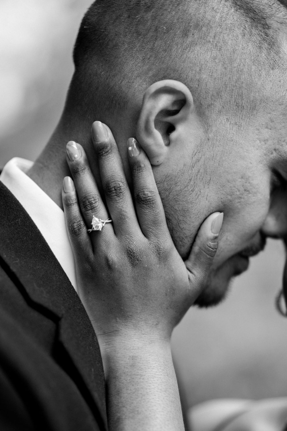Black and white portrait showing hand with engagement ring against face.