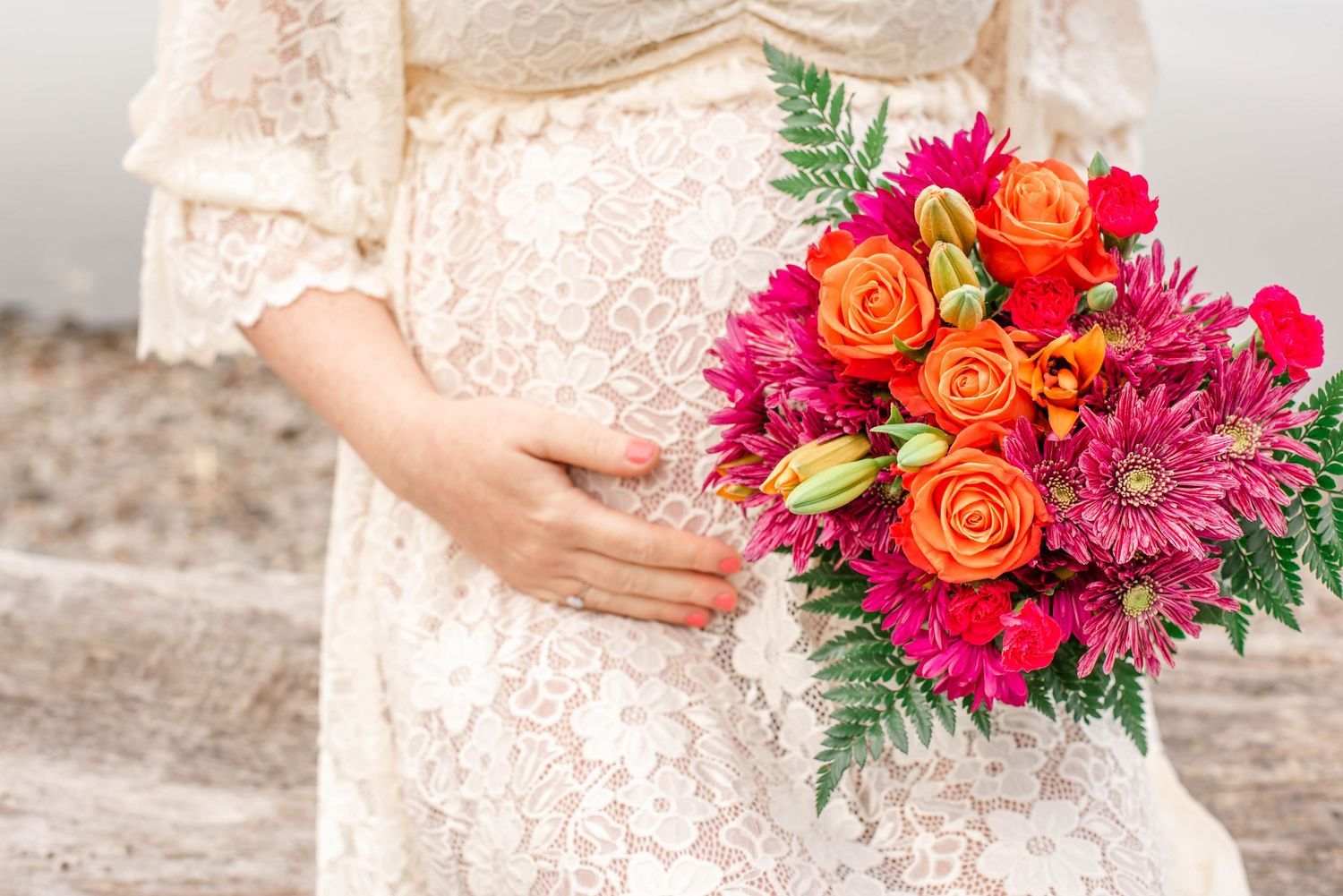 Pregnancy photoshoot featuring a couple embracing outdoors near colorful flowers.