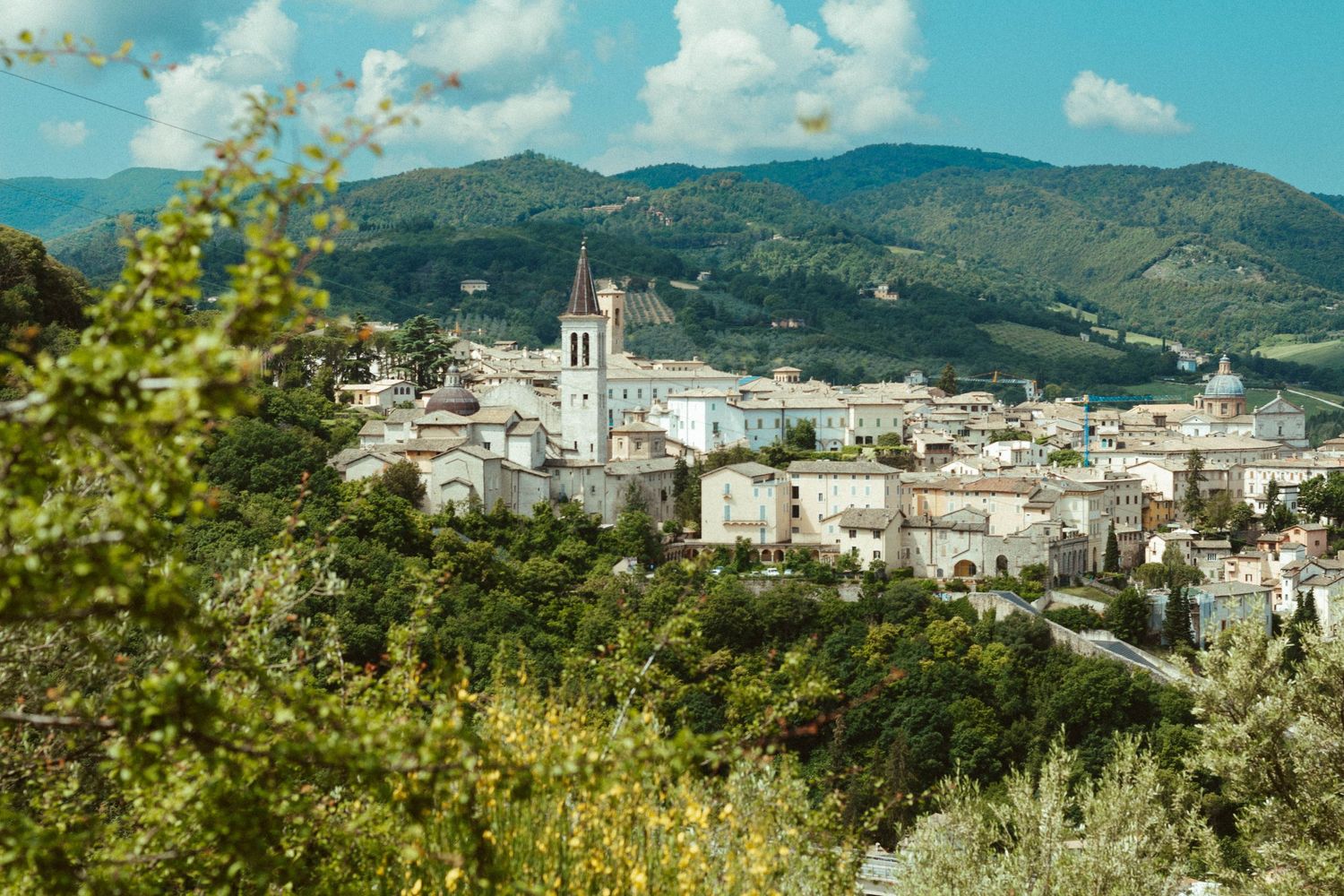 Scenic view of a Mediterranean town nestled in mountains with prominent church tower under blue skies.