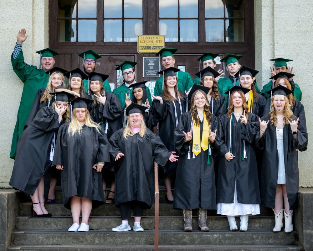 Graduates in black caps and gowns gather on steps for a celebratory group photo.