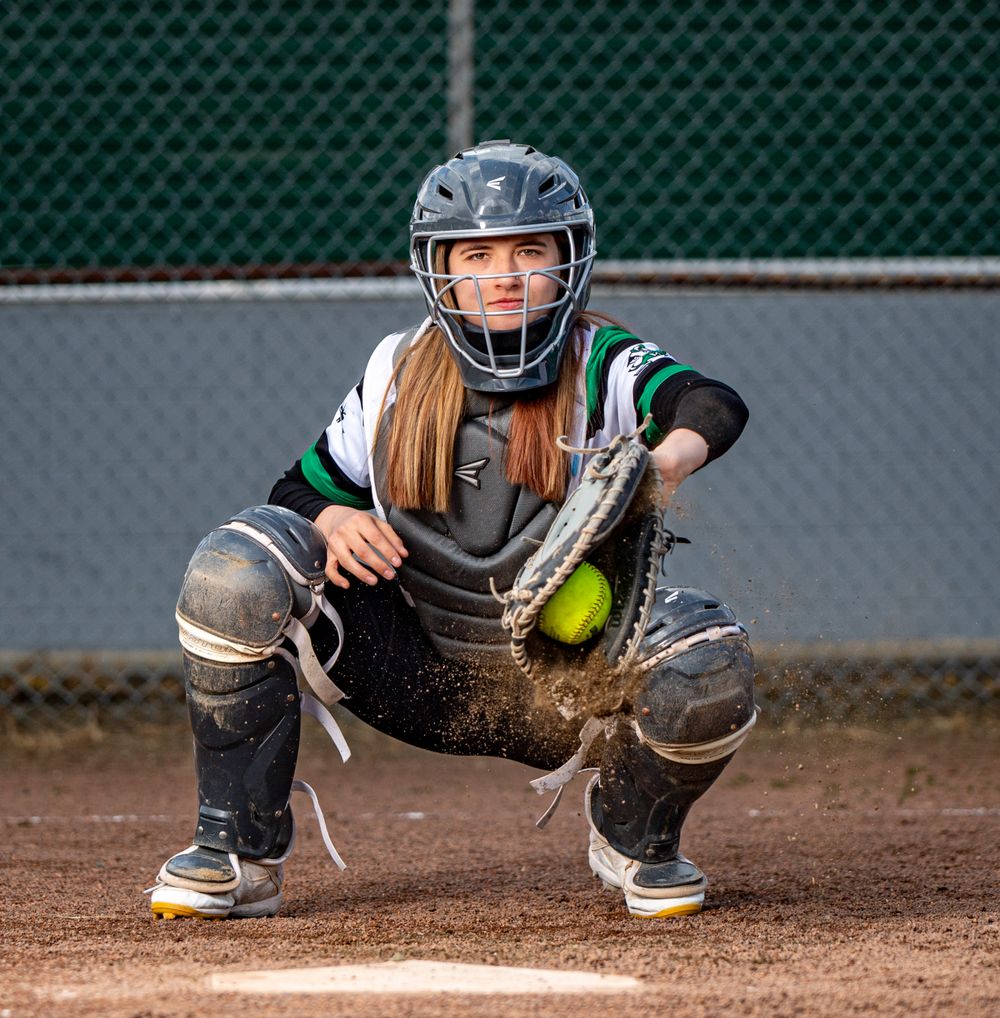 Softball catcher in protective gear ready to catch ball on field.