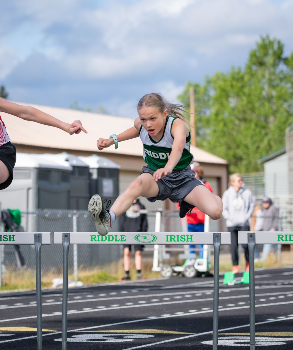 Track athlete leaping over hurdles during a competitive race wearing green Irish uniform.