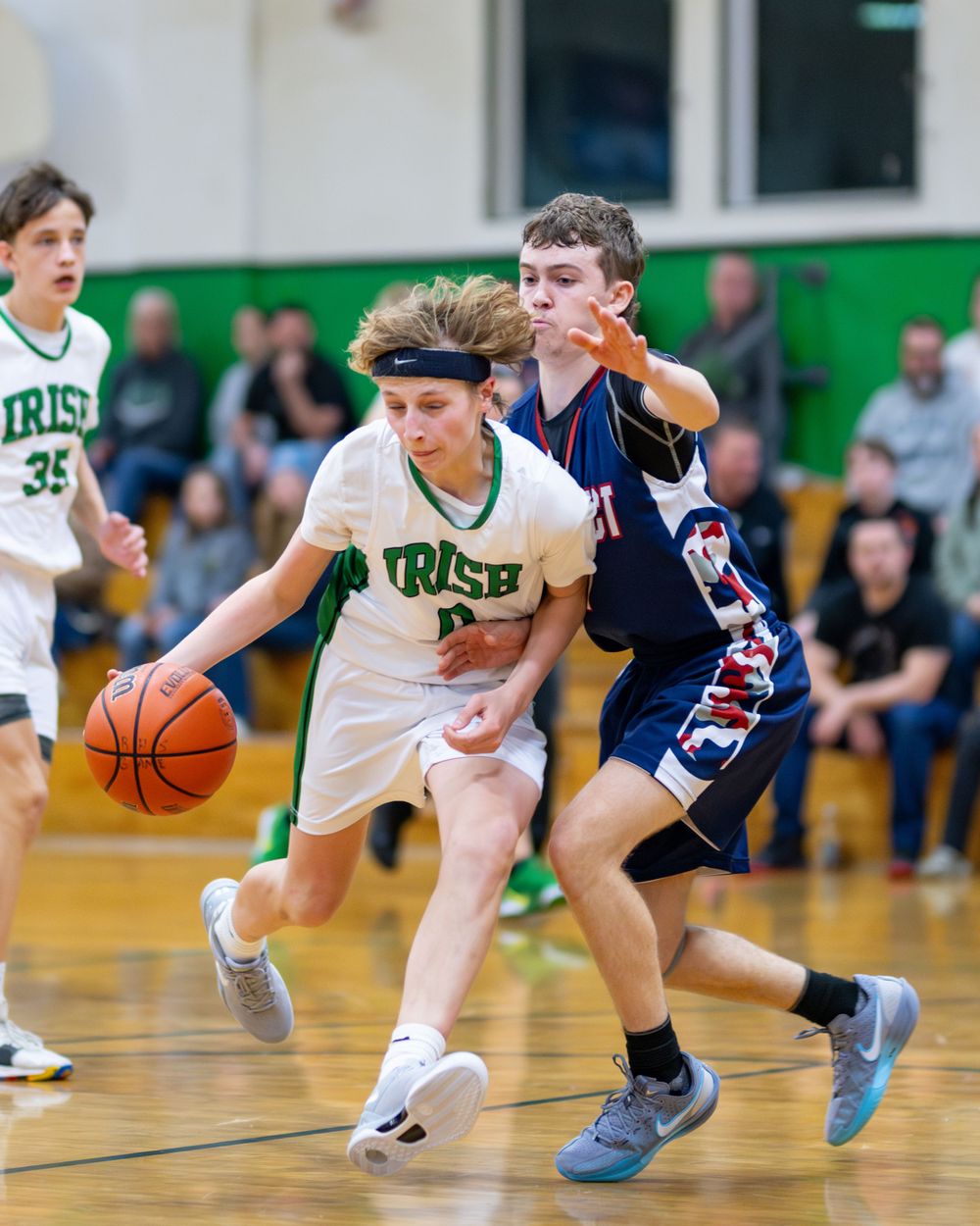 Two basketball players battle for possession during an intense high school game between Irish and their opponents.