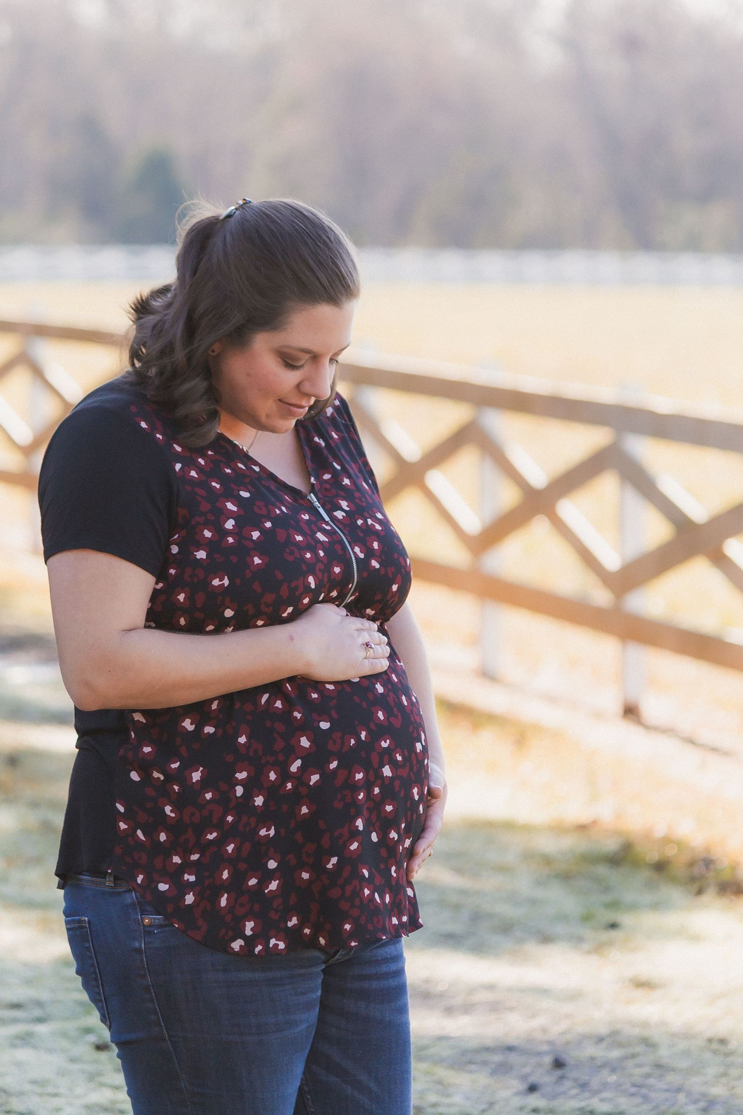 Pregnant woman in floral top holding her baby bump outdoors in golden sunlight.