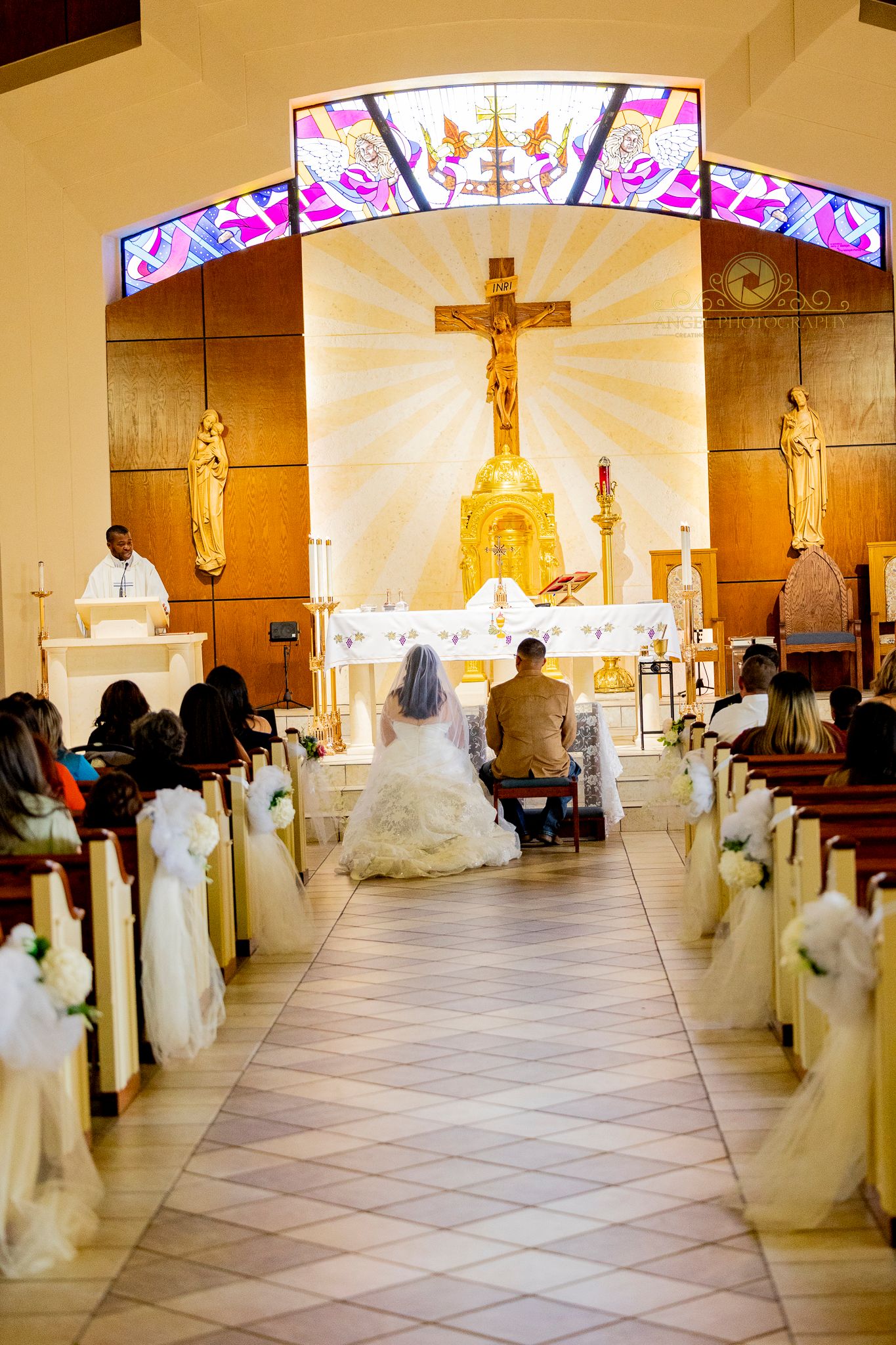 Church interior during wedding ceremony with illuminated crucifix and decorated aisle.