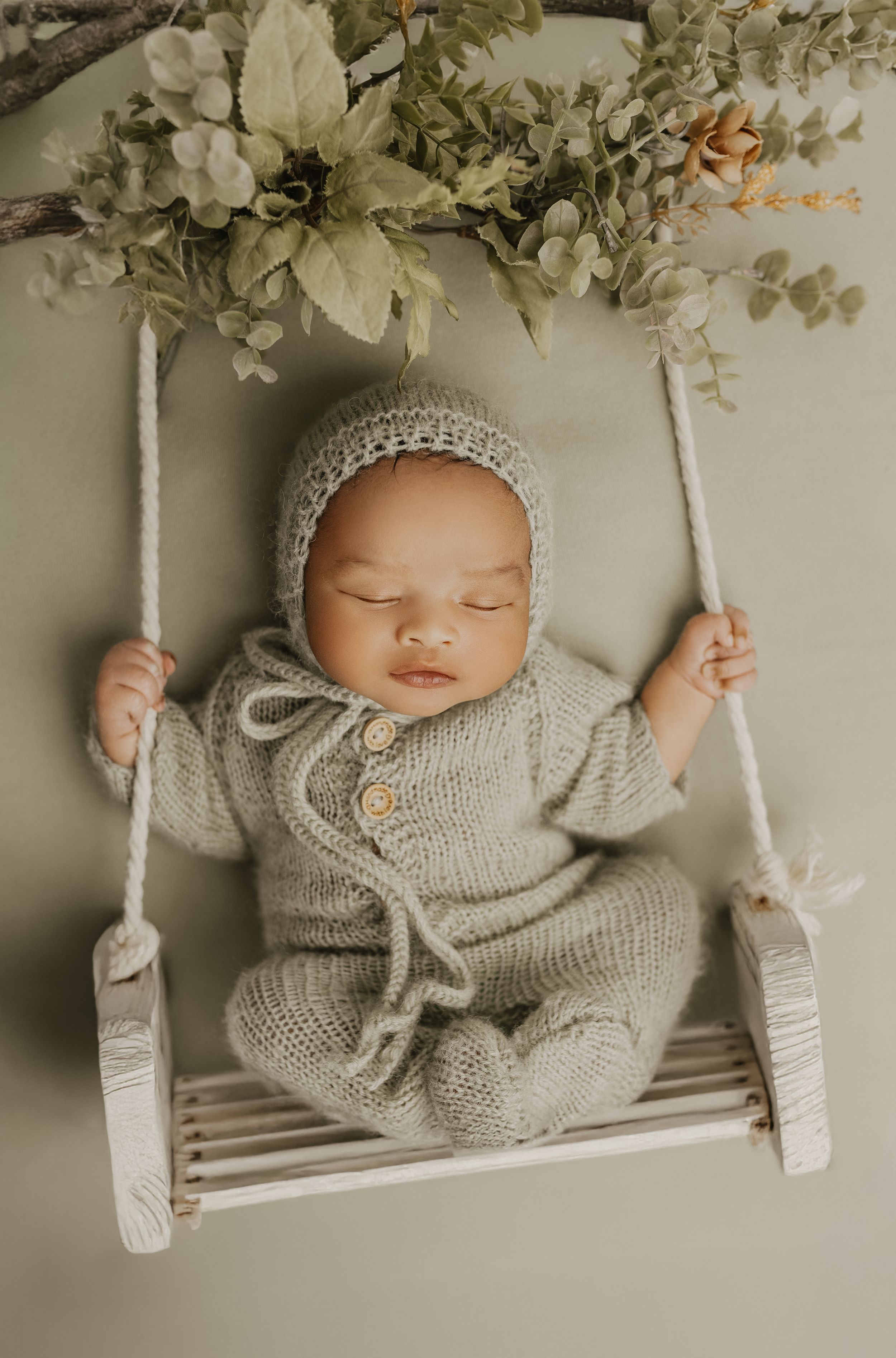 Sleeping baby in knit outfit on a wooden swing with floral decorations.
