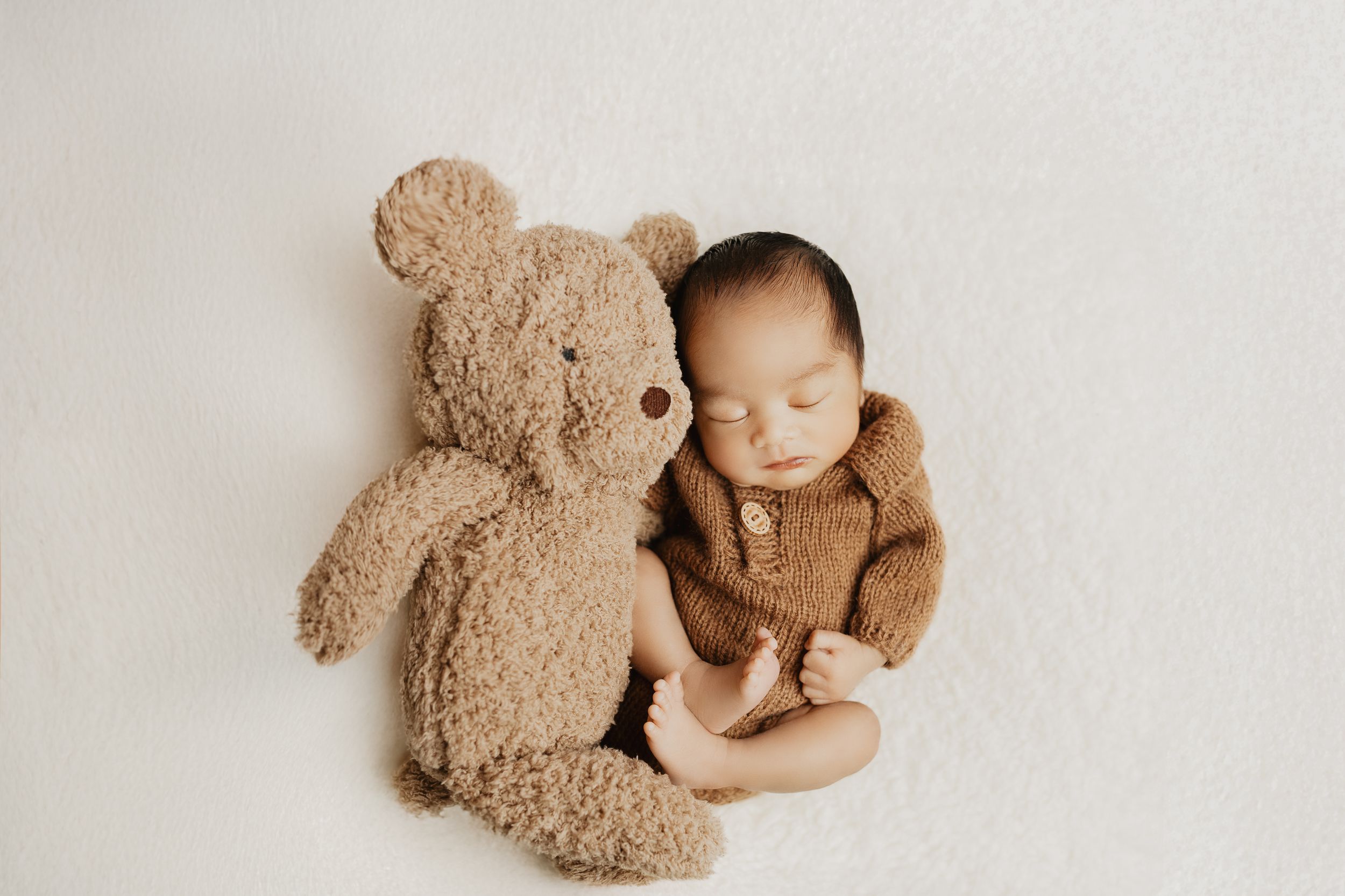 Minimalist newborn portrait with plush teddy bear against white background.