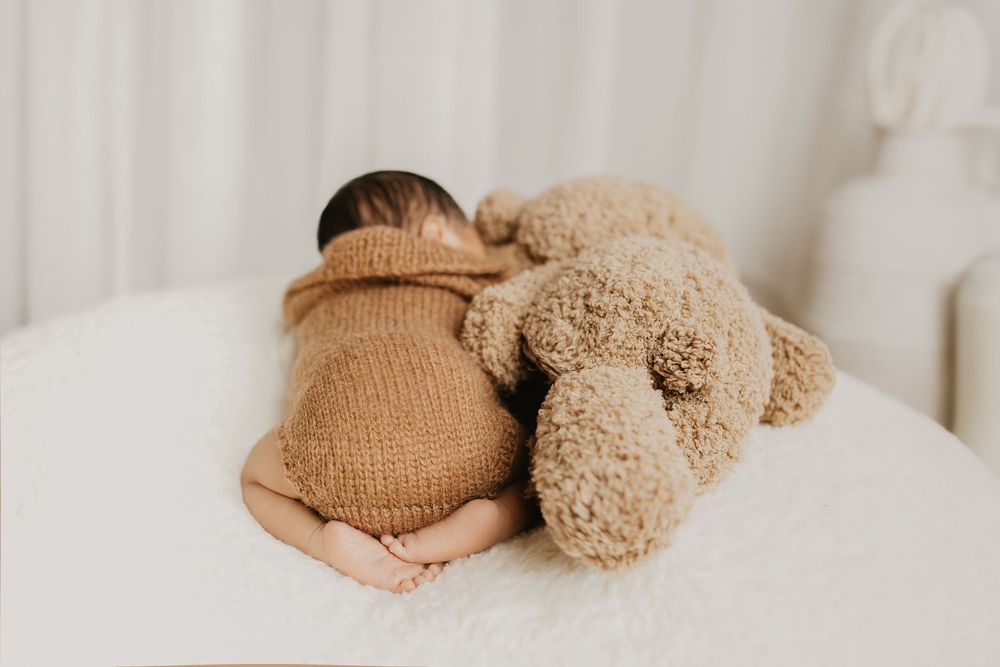 Newborn photography setup with soft brown teddy bear and knitted accessories.