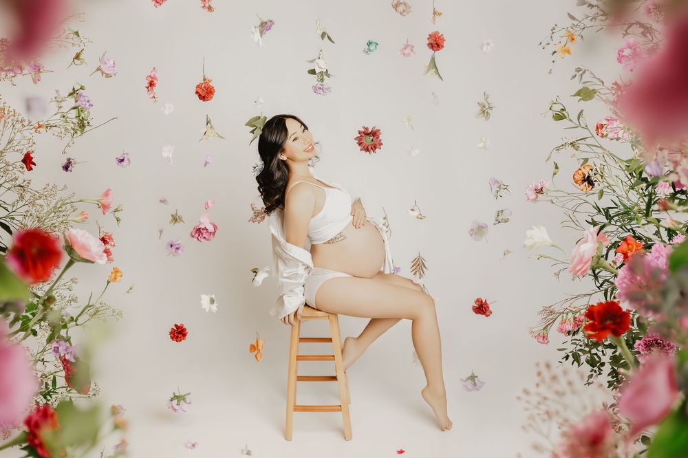 Whimsical maternity photo with floating flowers and wooden chair.